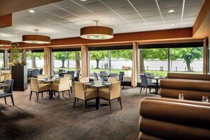 A restaurant with tables and chairs, large windows, and a view of a body of water. - Delta Hotels by Marriott Sault Ste. Marie Waterfront (Sault Ste. Marie)