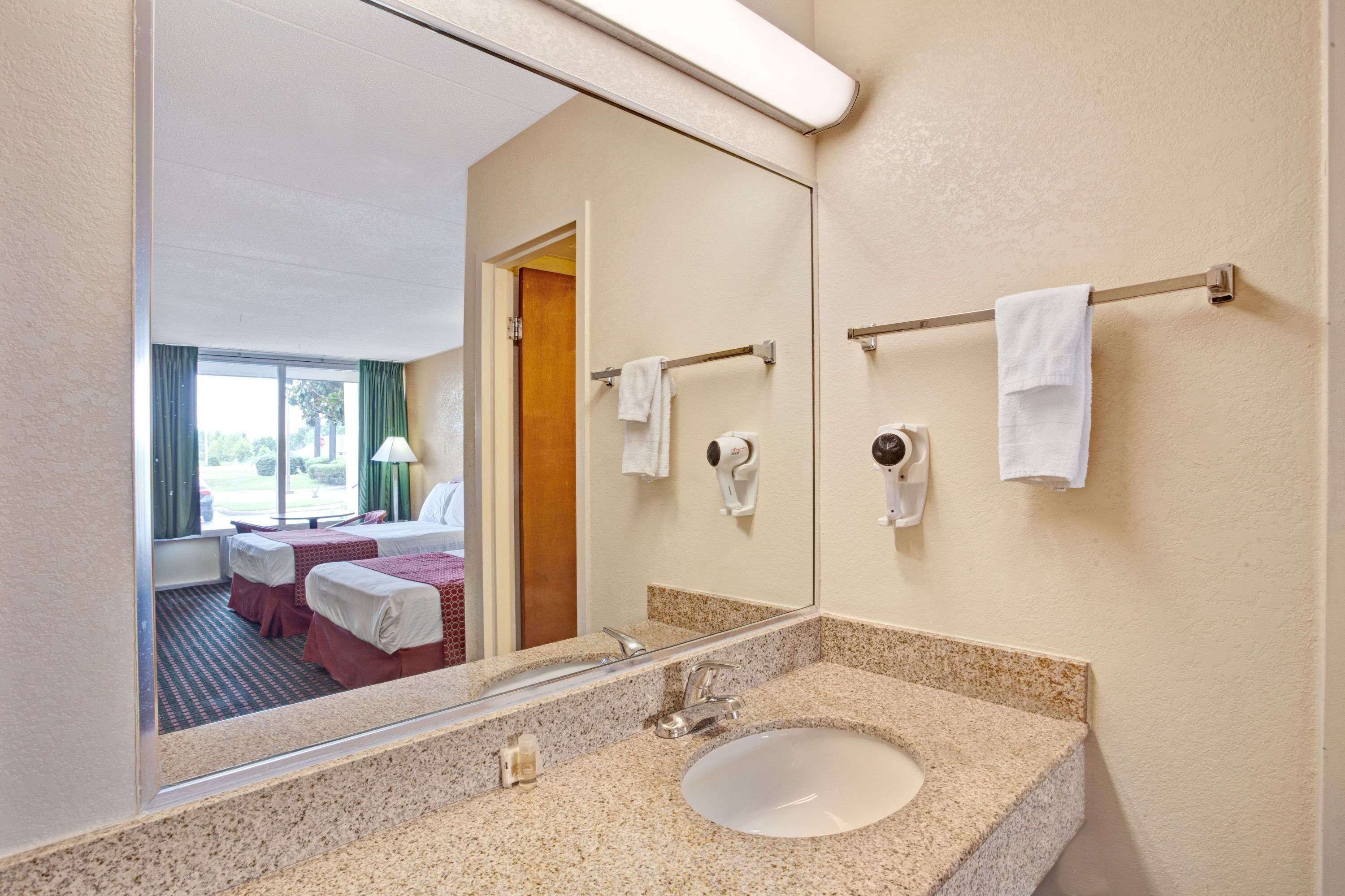 Une salle de bain d’hôtel avec un lavabo doté d’un plan de travail en granit, un grand miroir et deux serviettes suspendues à des porte-serviettes.