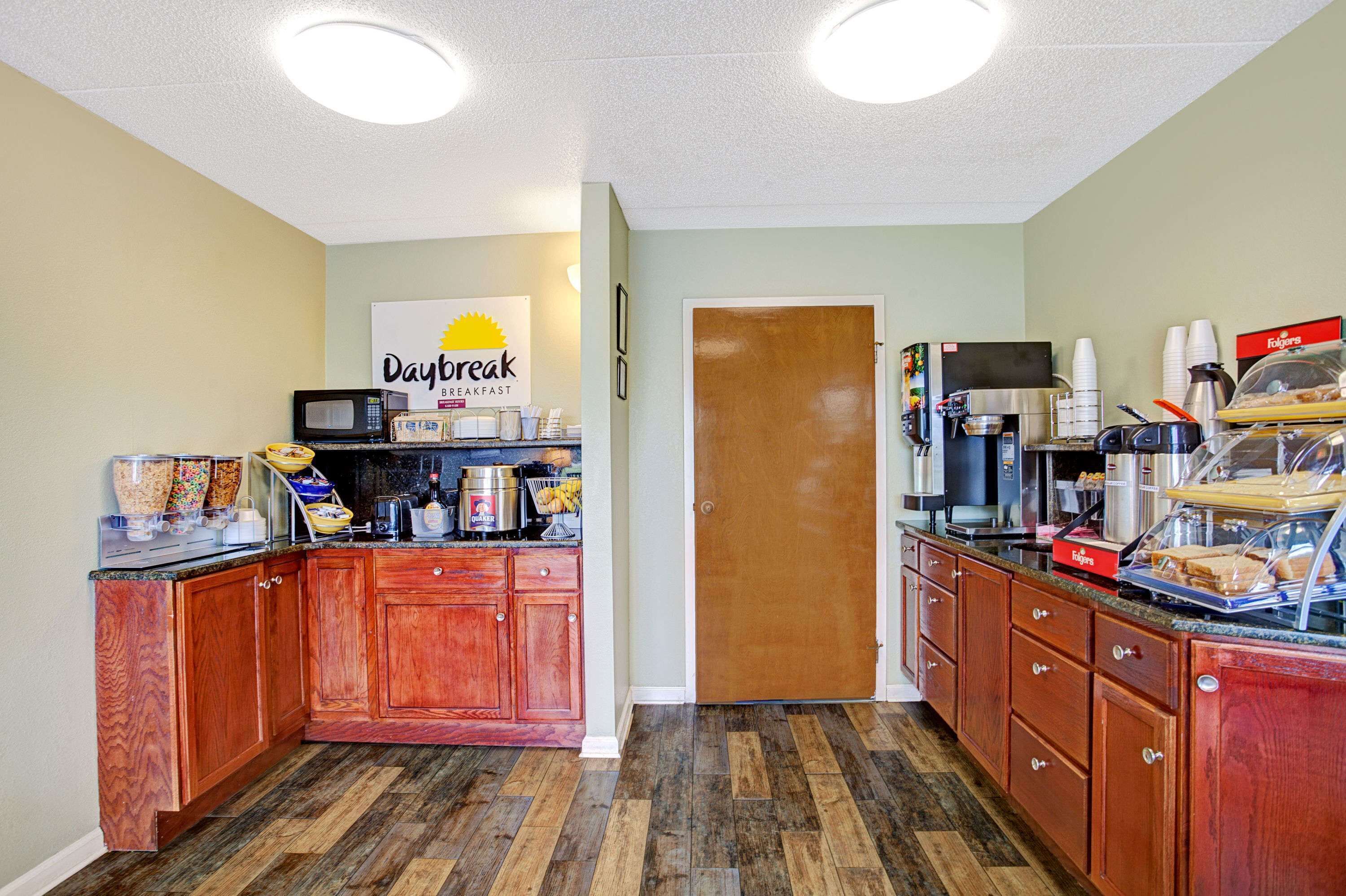 A breakfast area with wooden cabinets, a microwave, coffee machines, and a sign for Daybreak Breakfast.