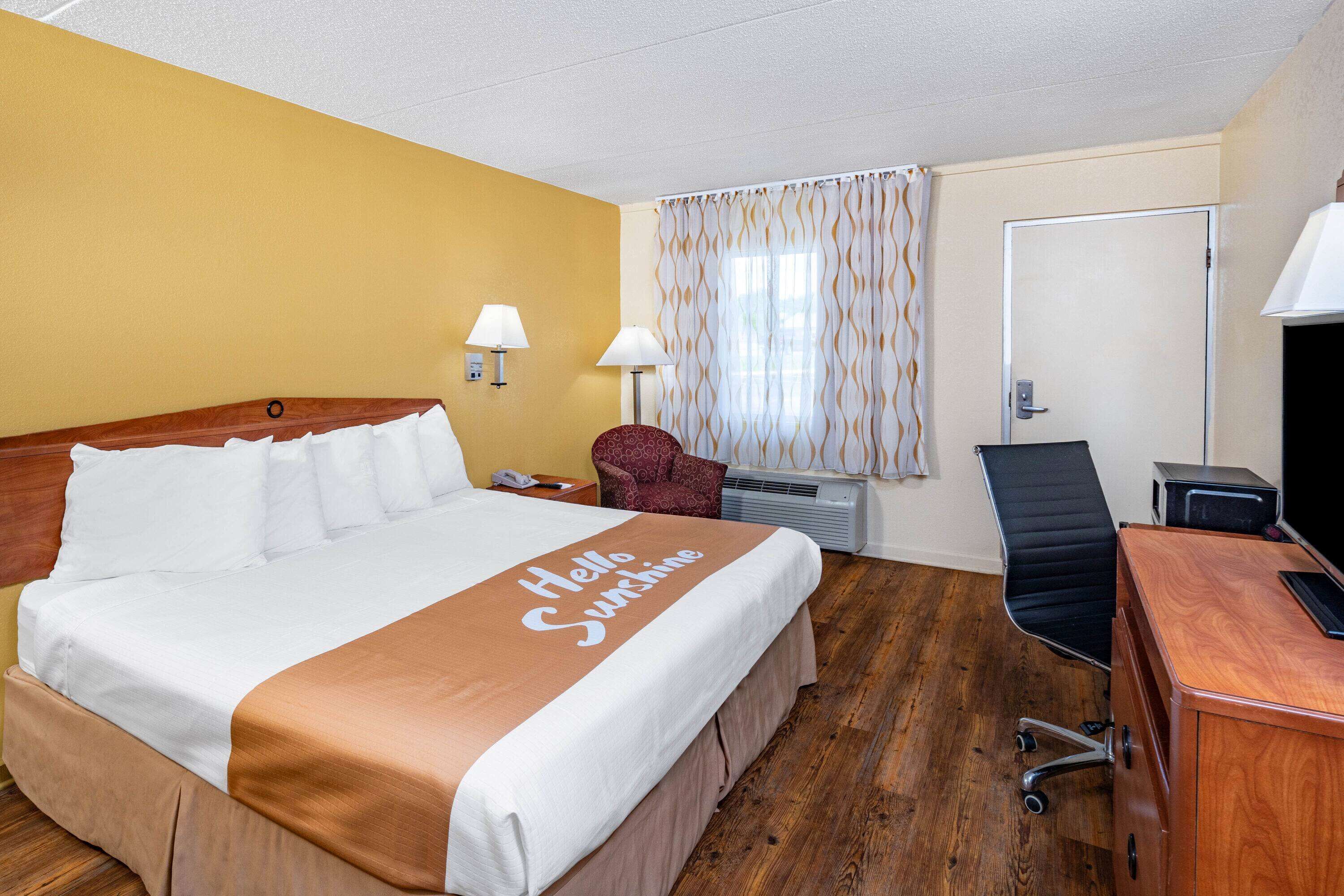 A hotel room with a bed, a desk, a chair, a lamp, a curtain, and a door.