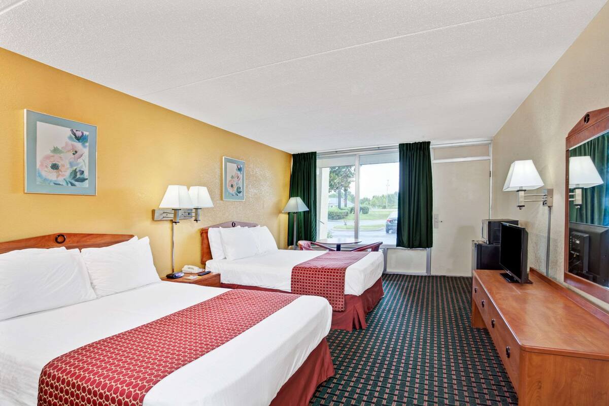 A hotel room with two beds, a desk, a TV, and a window with curtains.