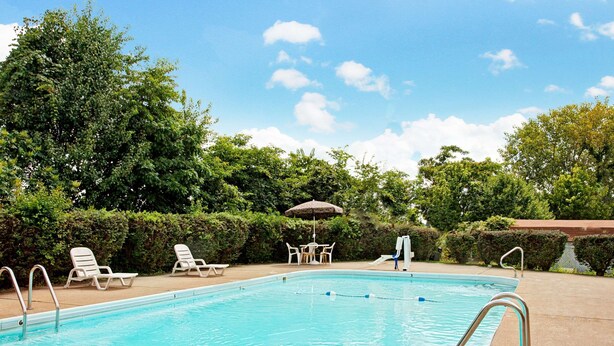 A swimming pool with lounge chairs and a table with umbrellas. - Days Inn by Wyndham Clarksville TN (Clarksville)