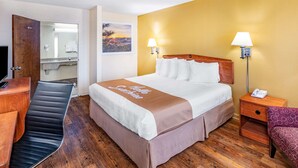 A hotel room with a bed, bedside lamps, a wooden nightstand, a chair, a desk, and a bathroom visible through an open door. - Days Inn by Wyndham Clarksville TN (Clarksville)