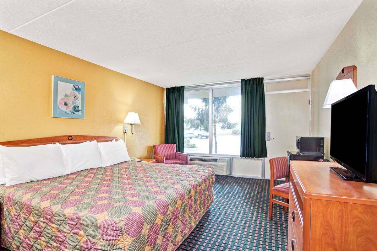 A hotel room with a large bed, a desk with a television, a chair, a lamp, and a window with curtains.