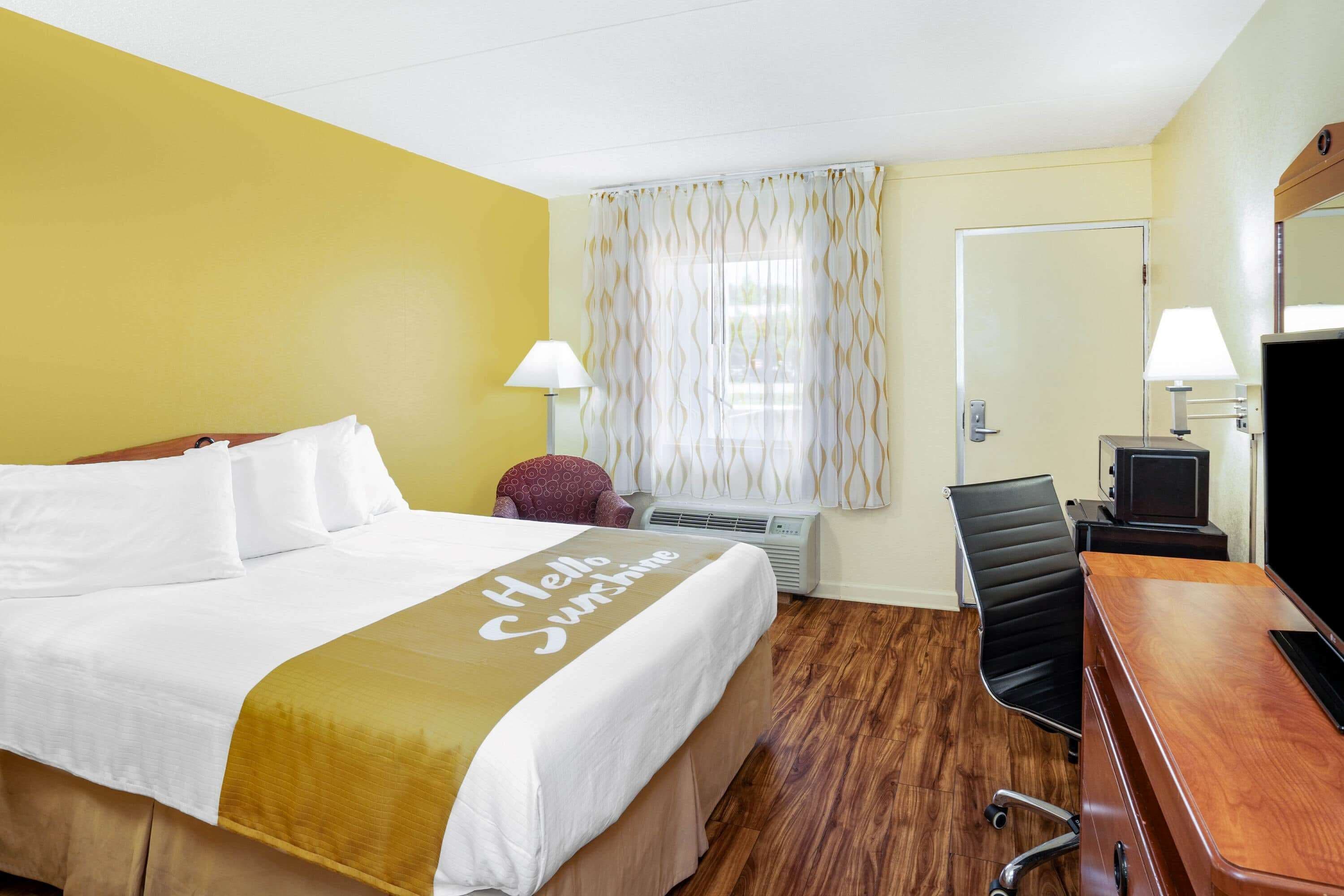 A hotel room with a bed, a desk, a chair, a TV, and a window with curtains.