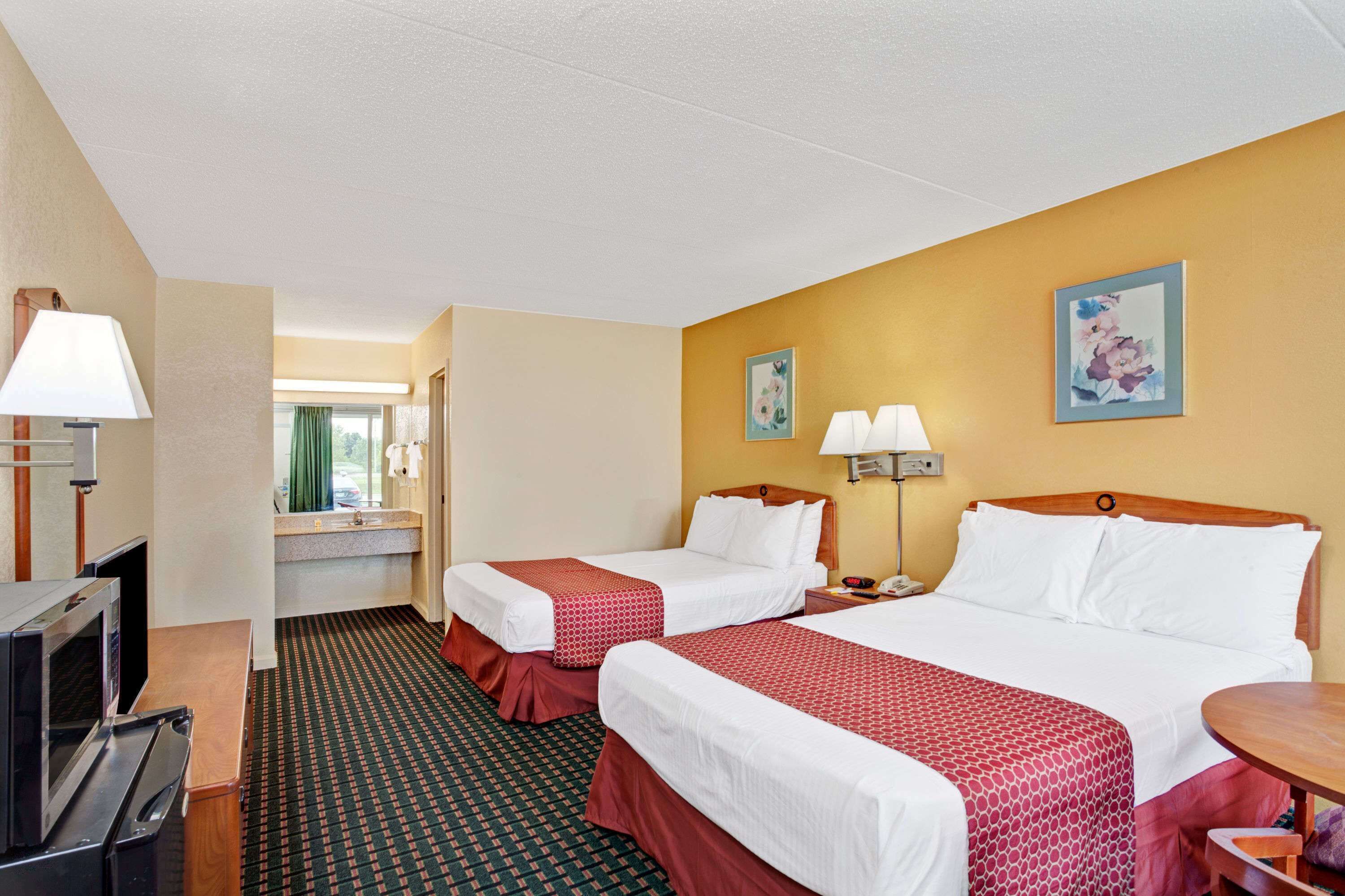 A hotel room with two beds, a desk, a microwave, a sink, and a mirror.