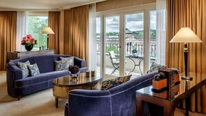 Una habitación de hotel moderna con un sofá azul, una mesa de centro de vidrio y vistas a la ciudad a través de amplios ventanales.