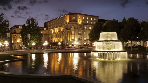 Un hotel histórico con una fachada imponente, una fuente central e un patio bien iluminado.