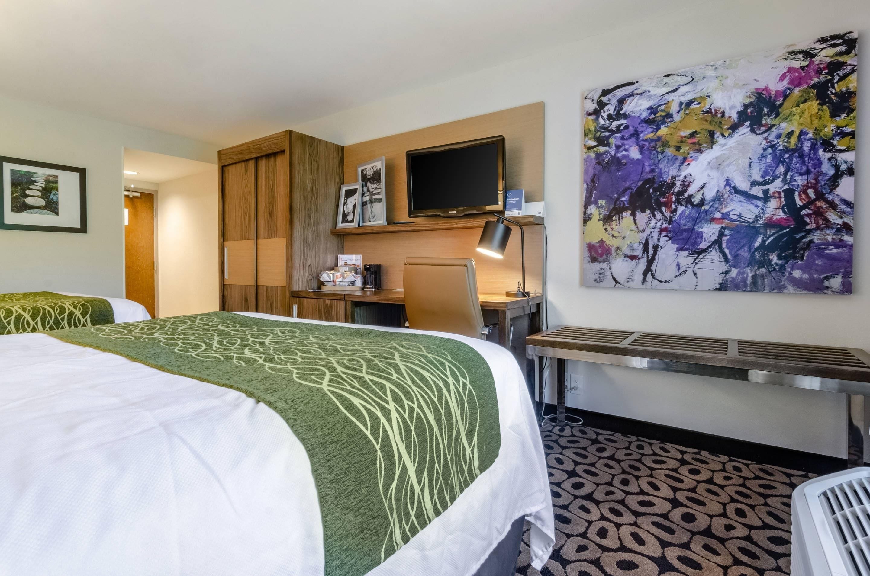 Habitación de hotel con cama, escritorio, silla y un cuadro abstracto grande en la pared.