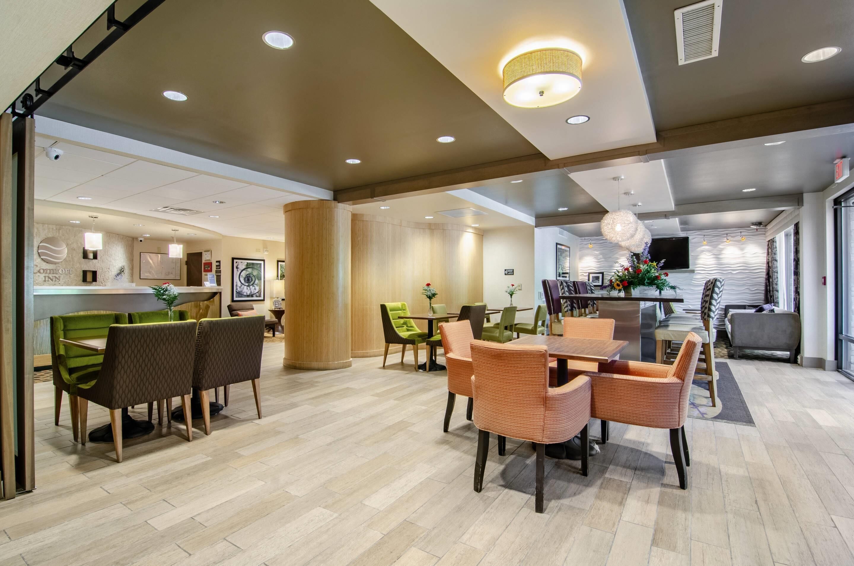 A hotel lobby with a dining area, a reception desk, and a modern kitchen in the background.