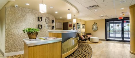 A reception area with a wooden reception desk, a potted plant, and a patterned carpet.