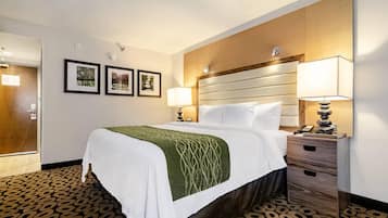 Quarto de hotel com cama, mesa de cabeceira, luminária e televisão presa à parede.