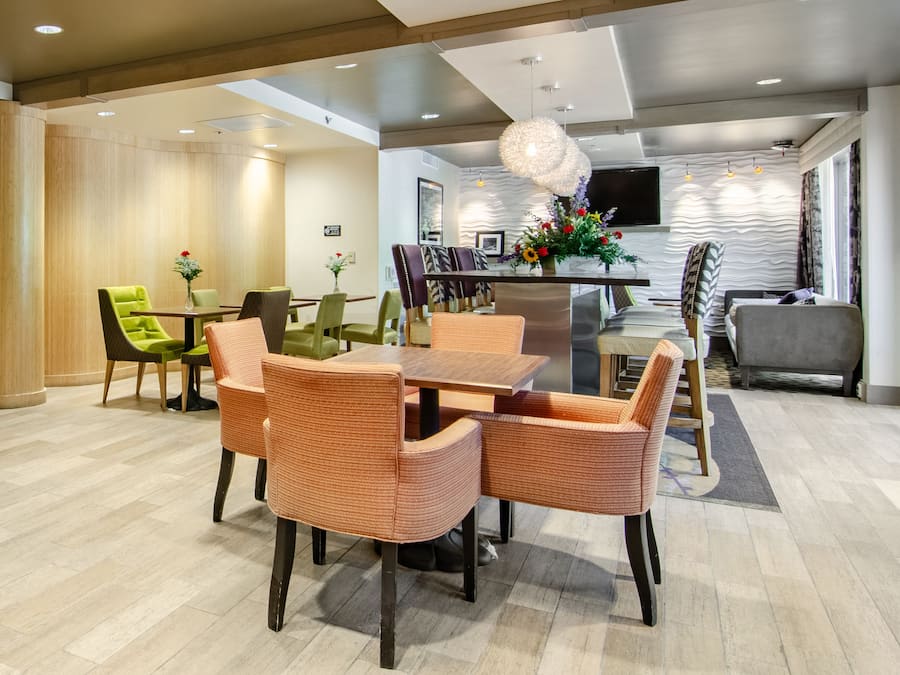 Uma sala de jantar moderna com uma mesa central, rodeada por cadeiras de vime, e um espaço de estar com um sofá e poltronas.