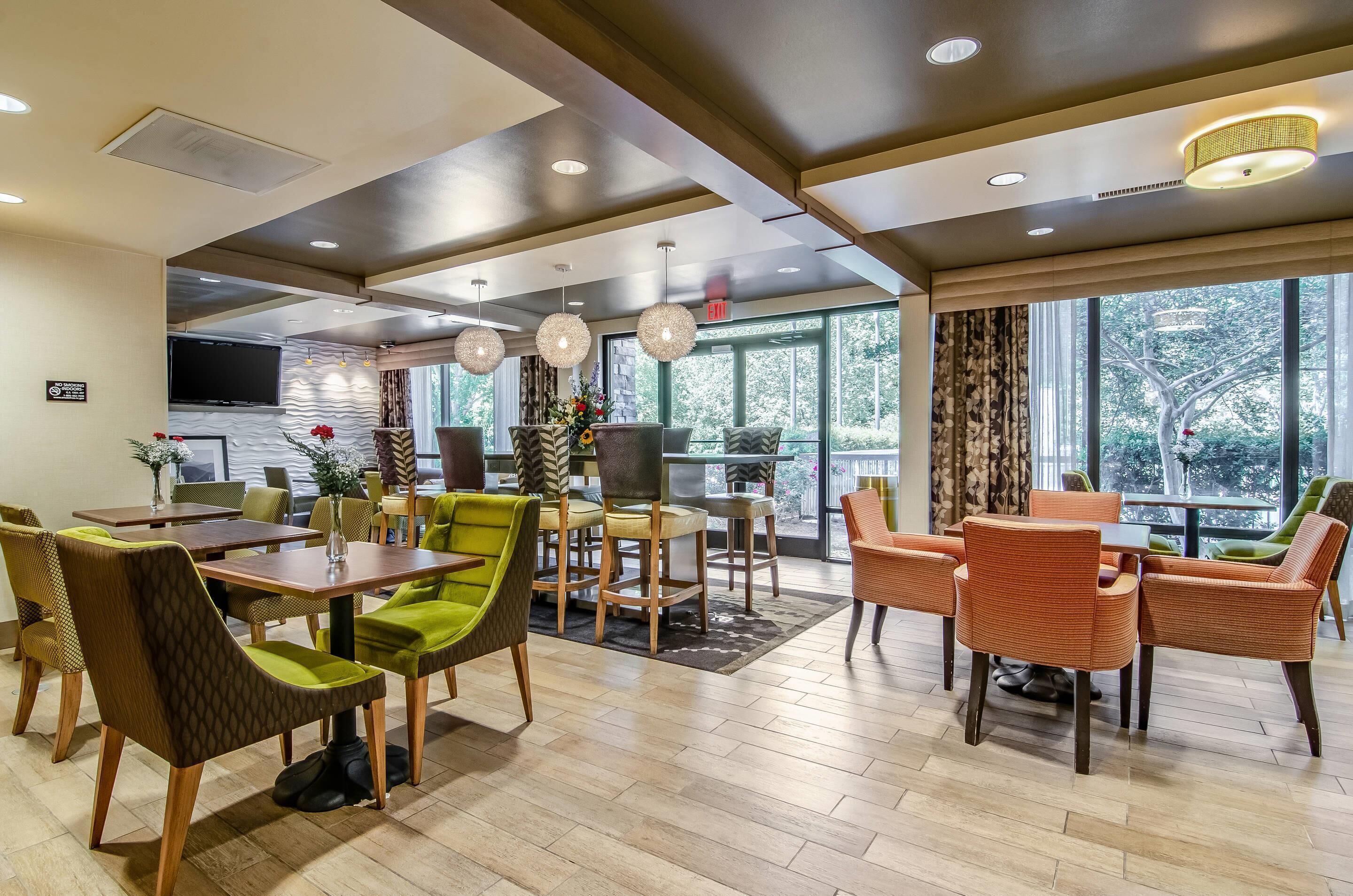 A modern hotel lobby with a dining area, large windows, and a flat-screen TV.