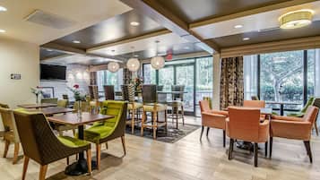 A modern hotel lobby with a dining area, large windows, and a flat-screen TV.