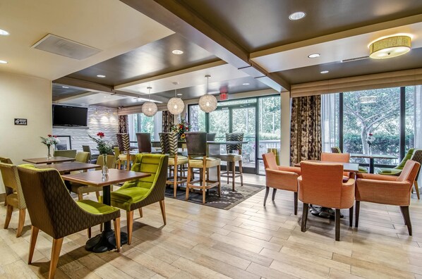 A modern hotel lobby with a dining area, large windows, and a flat-screen TV.