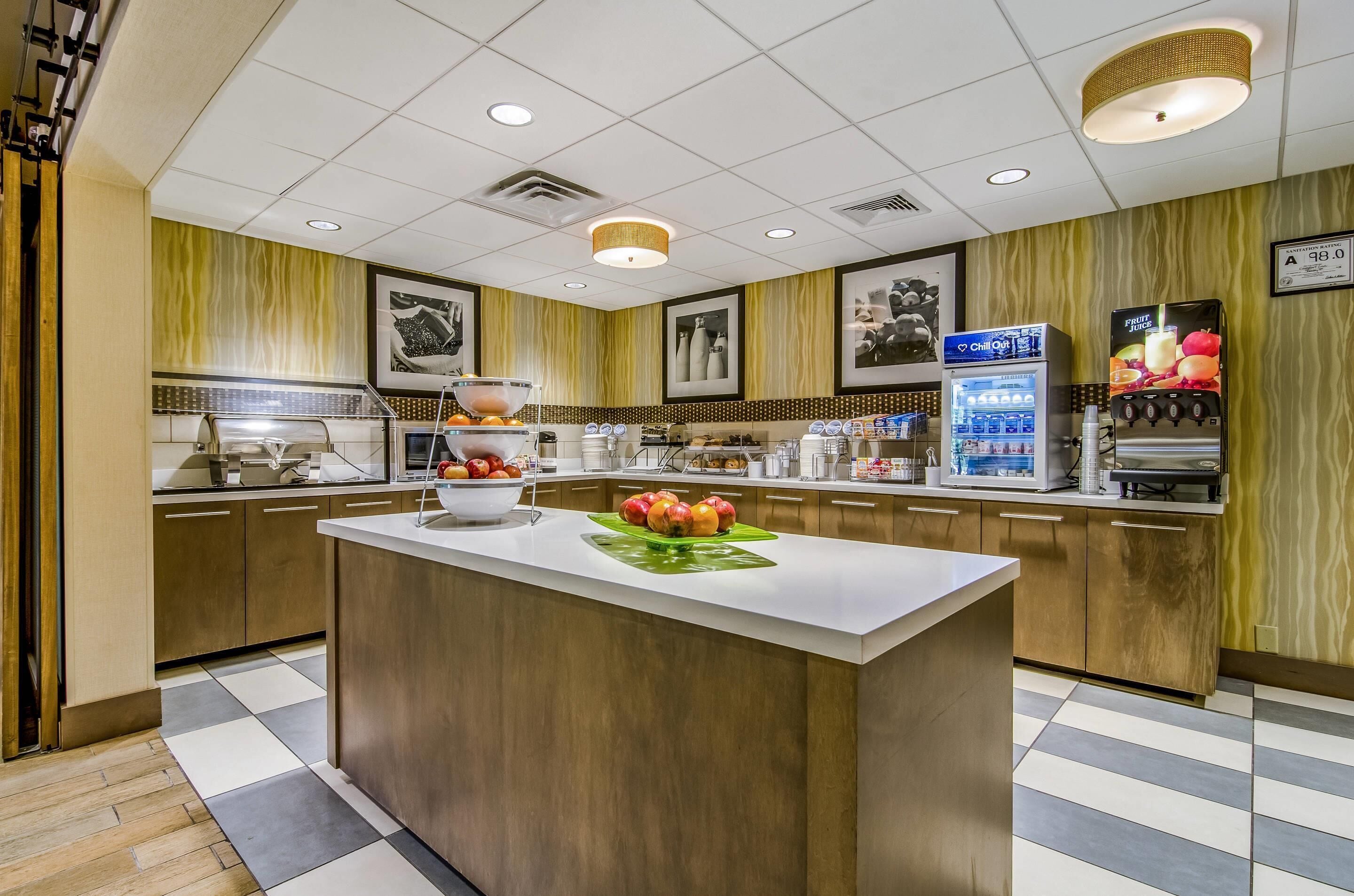 Una cocina de hotel con una isla central, un refrigerador y un dispensador de jugo de frutas.