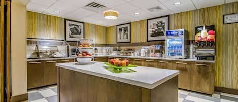 A hotel kitchen with a central island, a refrigerator, and a fruit juice dispenser.