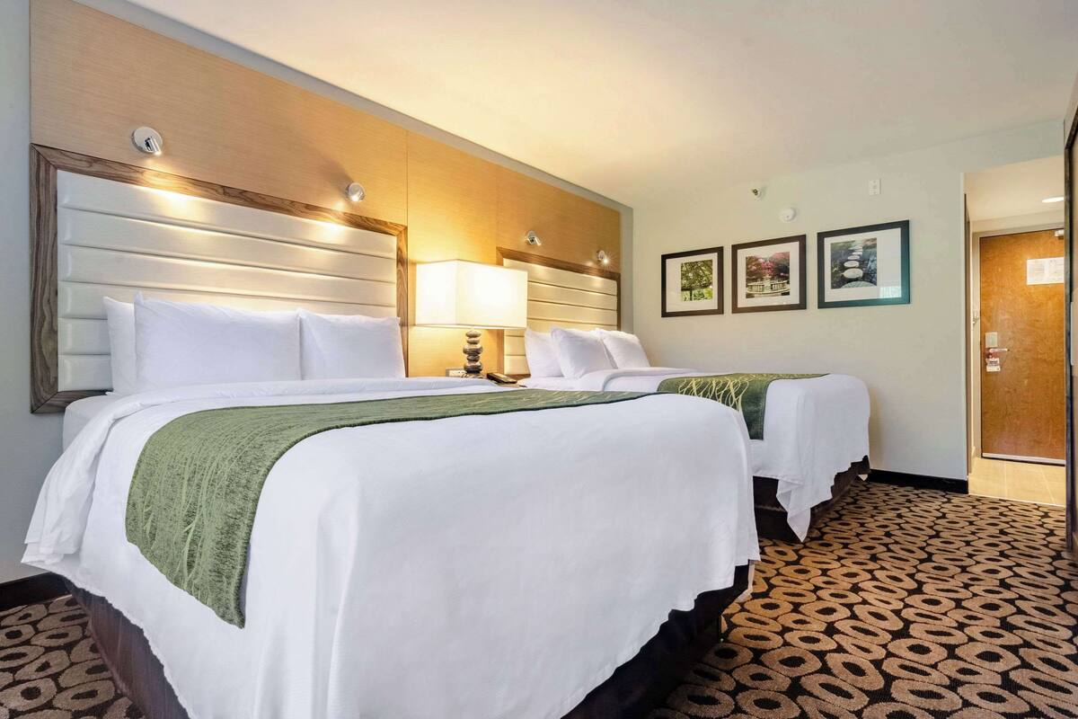 A hotel room with two beds, a wooden headboard, a patterned carpet, and framed pictures on the wall.