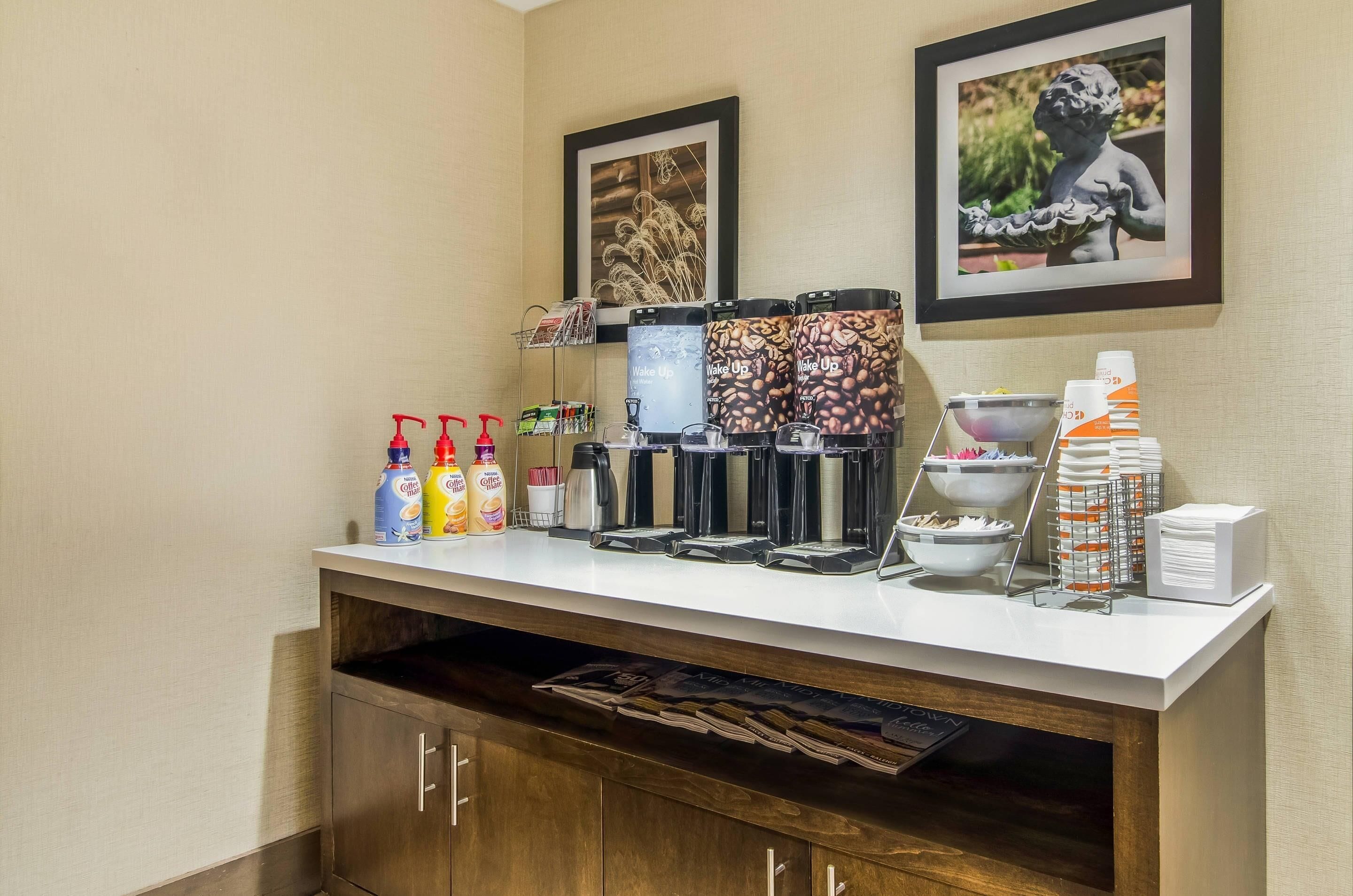Una estación de café autoservicio con varias máquinas de café, dispensadores y una selección de botellas de leche para café.