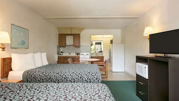 A hotel room with two beds, a kitchenette, a television, and a dining area.