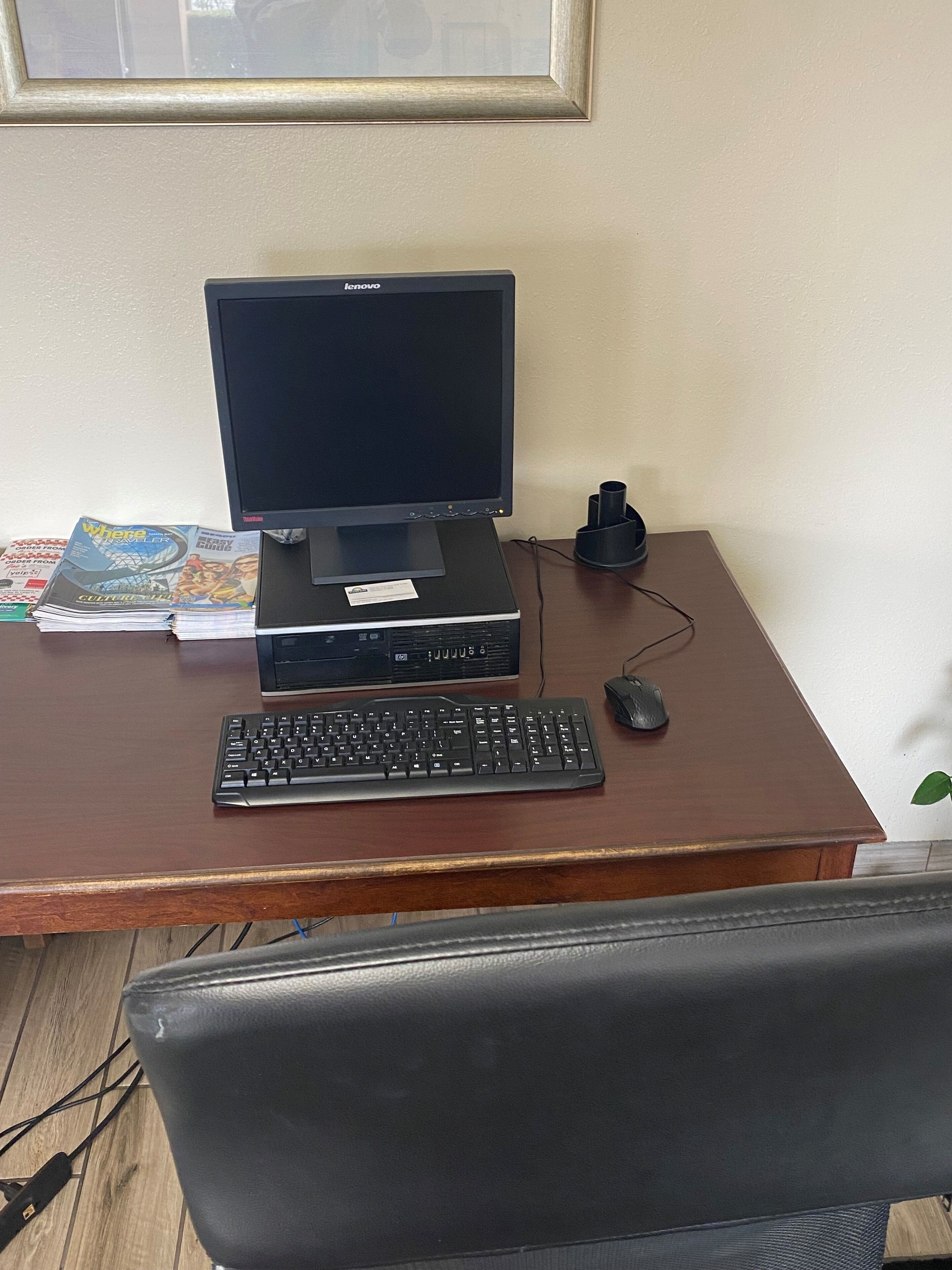 Un escritorio con un monitor Lenovo, un teclado, un ratón y una pila de revistas.
