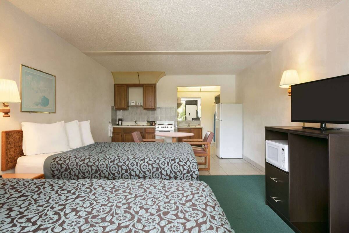 Ein Hotelzimmer mit zwei Betten, einer Küchenzeile, einem Essbereich und einem Fernseher.