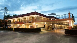 Un hotel de dos pisos con techo rojo, varios balcones y un área de entrada cubierta.