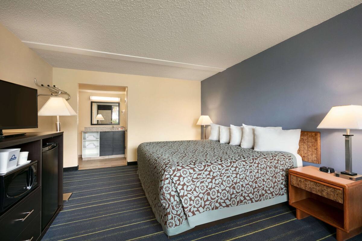 Ein Hotelzimmer mit einem Bett, Nachttischlampen, einem Fernseher, einem Schreibtisch und einem Spiegel.