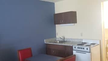 Una cocina pequeña y funcional con estufa, lavamanos y dos sillas rojas junto a una mesa.