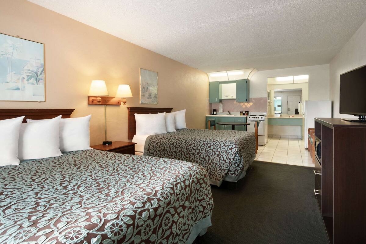 Ein Hotelzimmer mit zwei Betten, einem Schreibtisch, einem Stuhl, einem Fernseher und einem durchgegangenen Tür erkennbaren Badezimmer.
