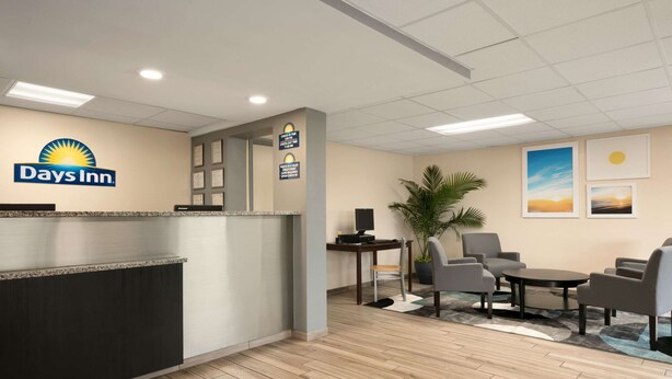 Zona de recepción con el letrero de Days Inn, un mostrador de recepción, una computadora, un área de descanso con sillas y una mesa, y cuadros en la pared.