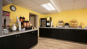 Una cocina con pared amarilla, muebles negros y piso de madera. Hay varios electrodomésticos y alimentos sobre la encimera.