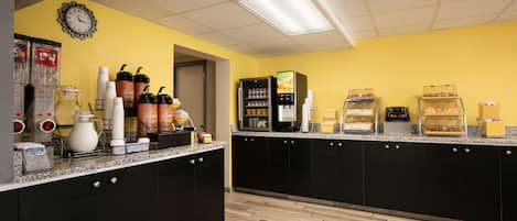 Una cocina con pared amarilla, muebles negros y piso de madera. Hay varios electrodomésticos y alimentos sobre la encimera.