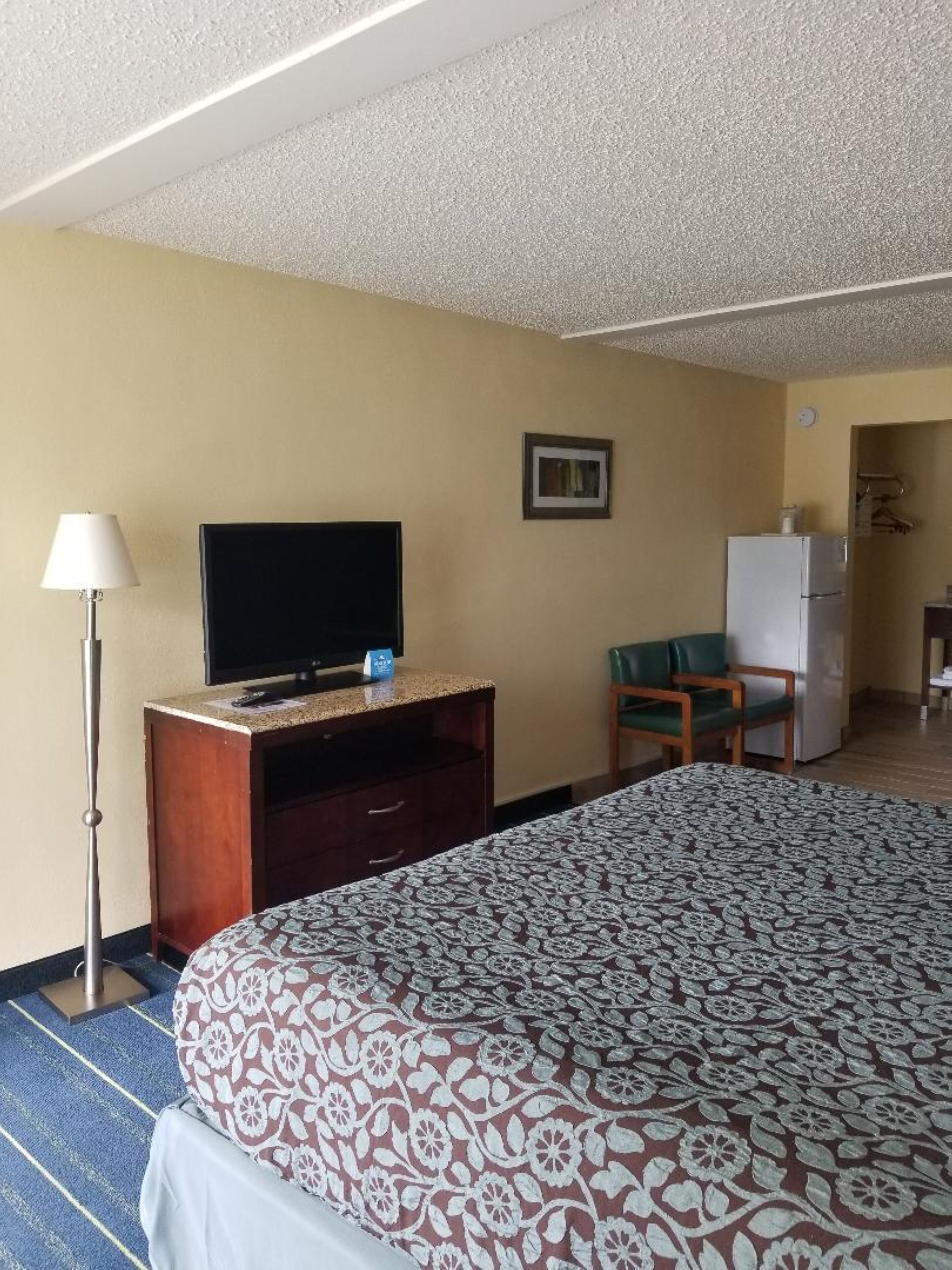 A hotel room with a bed, a television on a wooden stand, a desk, a chair, and a refrigerator.