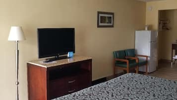 A hotel room with a bed, a television on a wooden stand, a desk, a chair, and a refrigerator.