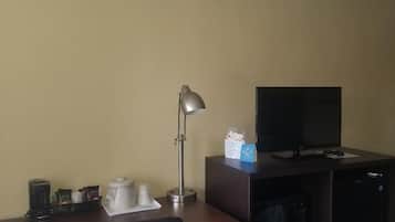 Une chambre d’hôtel de taille réduite, équipée d’un bureau, d’une chaise, d’une télévision, d’une machine à café et d’un four à micro-ondes.