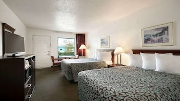 Ein Hotelzimmer mit zwei Betten, einem Fernseher, einem Schreibtisch und einem Fenster mit Blick ins Freie.