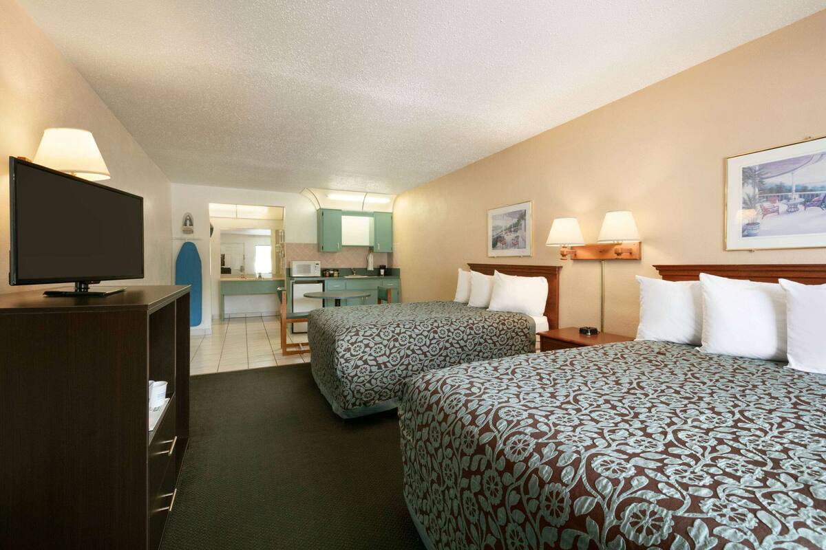 Ein Hotelzimmer mit zwei Betten, einem Fernseher, einem Schreibtisch und einer Küchenzeile.