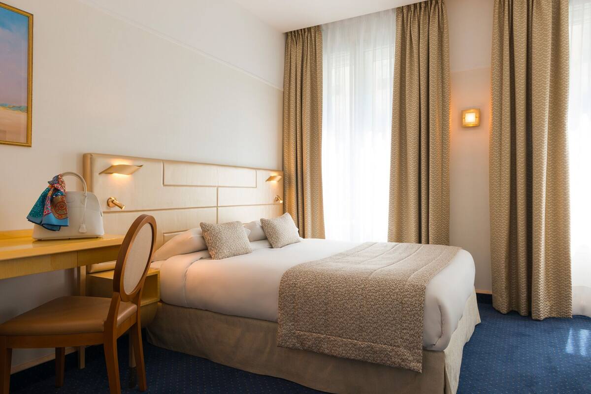 Una habitación de hotel con cama, escritorio, silla y mesita de noche.