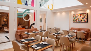 A modern dining area with high ceilings, geometric wall art, and a mix of seating options including tables and sofas. - Atlantic Hotel (Paris)