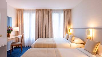 Une chambre d’hôtel avec deux lits, un bureau avec une lampe, une chaise et un vase de fleurs.