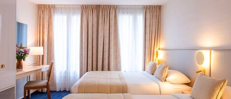 A hotel room with two beds, a desk with a lamp, a chair, and a vase of flowers.
