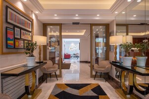 A modern hotel lobby with a central seating area, glass partitions, and a geometric patterned rug.