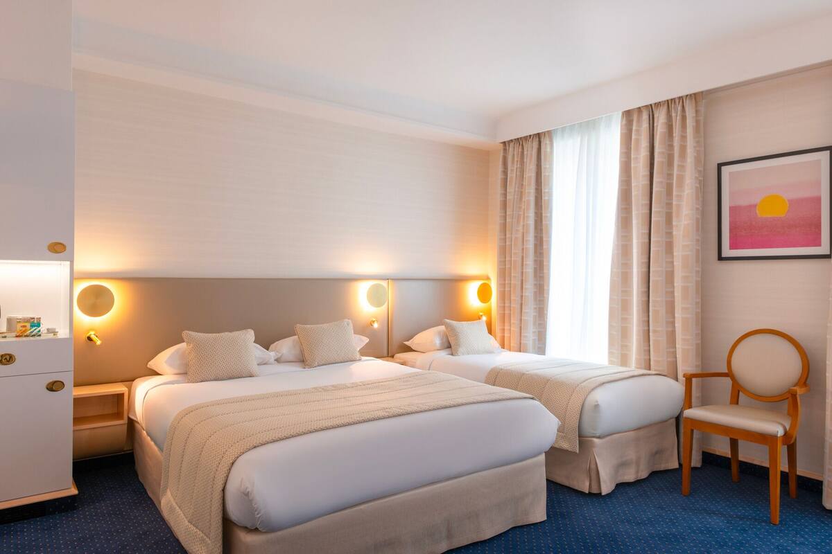 Una habitación de hotel con dos camas, un escritorio, una silla y un cuadro en la pared.