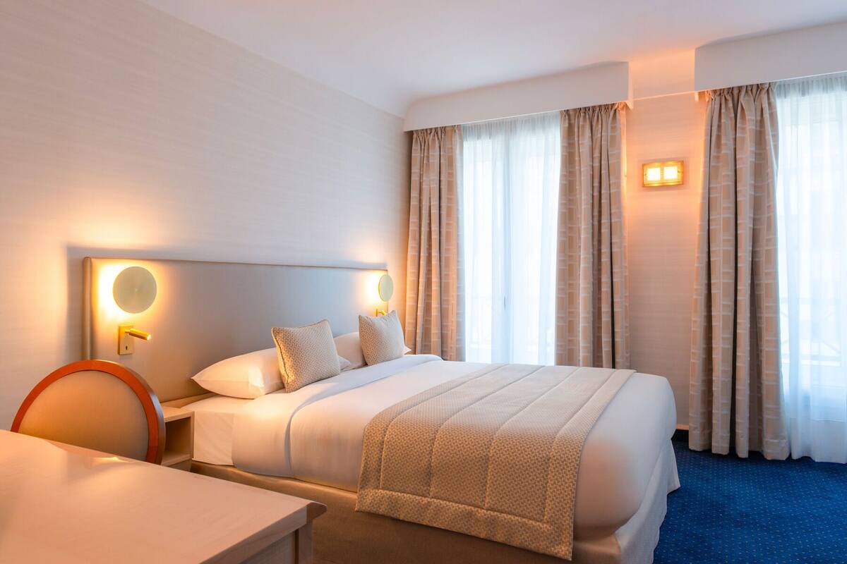 Una habitación de hotel con una cama grande, una mesita de noche, una silla y un escritorio.