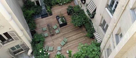 A courtyard with a wooden deck, green seating, and potted plants.