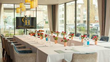 Un salón de conferencias en el Hotel Conrad Cambridge, con una larga mesa, sillas y una pantalla grande.