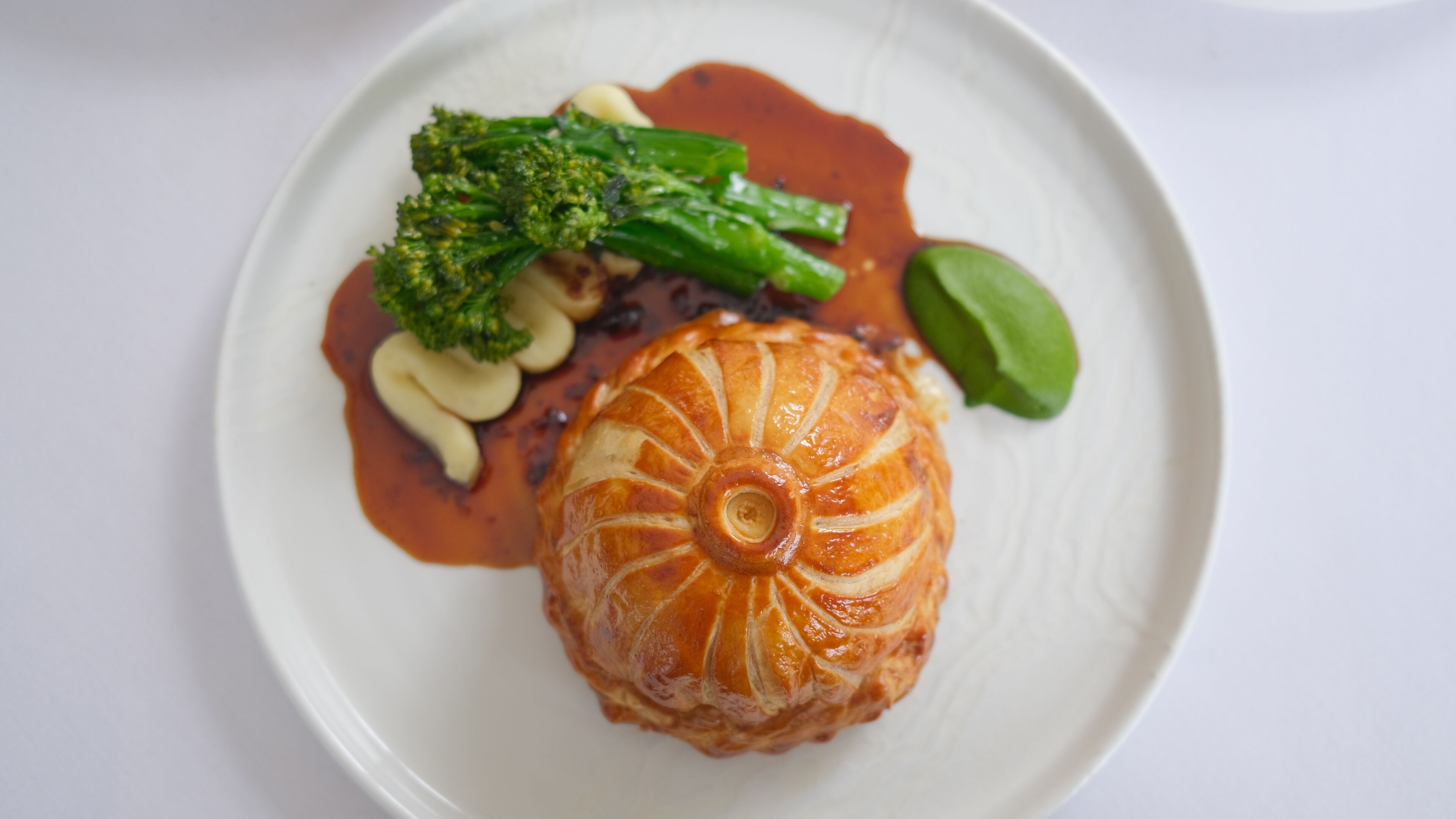 A plate with a pastry, broccoli, and a sauce.