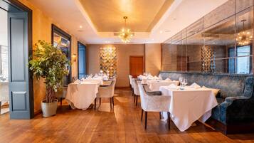A restaurant with wooden flooring, white tablecloths, and a large potted plant.
